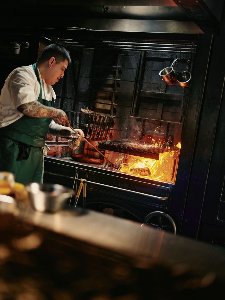A Fife Arms chef stoking the fire on the kitchen grill