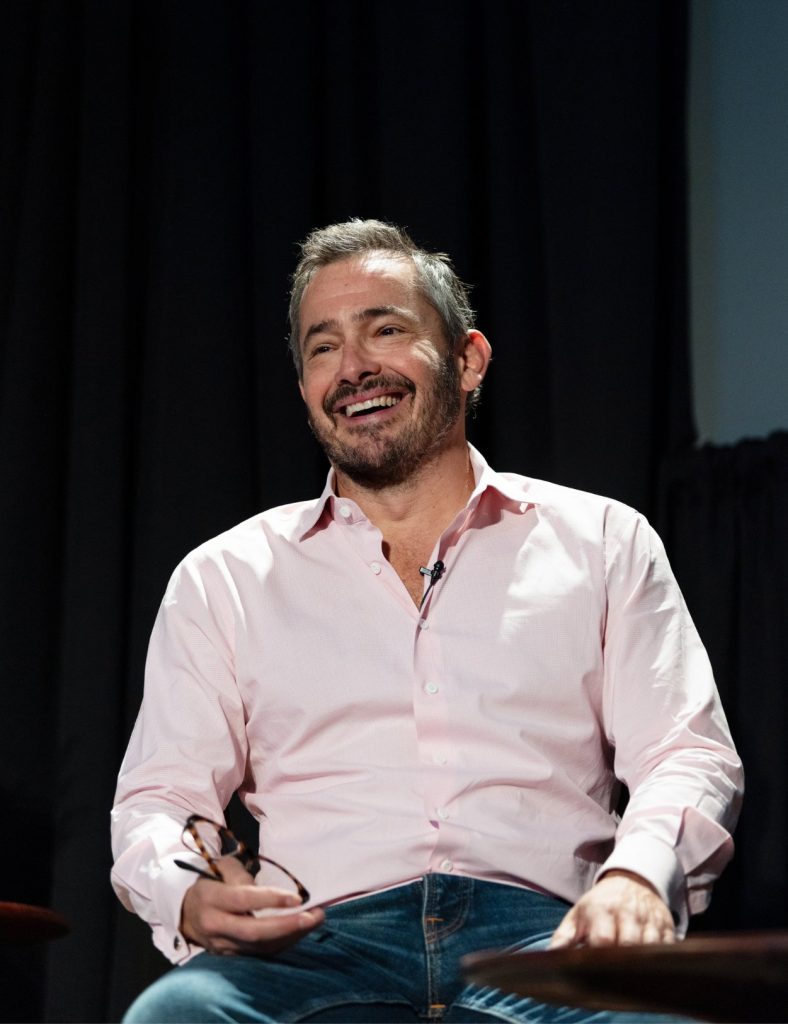 Giles Coren laughing on stage during a talk event.