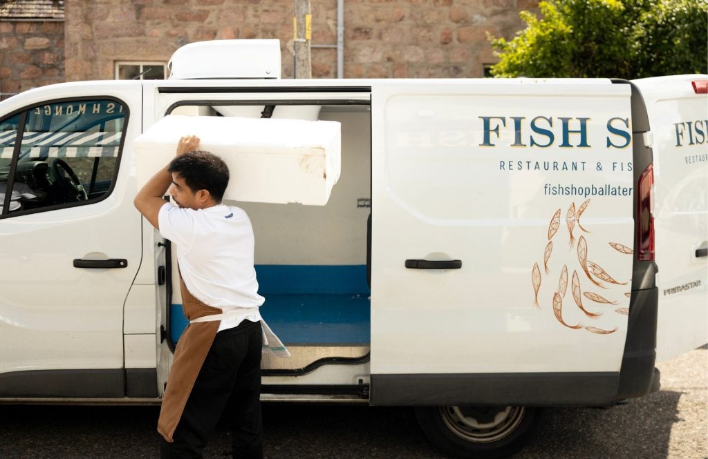 A man carrying fresh fish in a box from the Fish Shop branded van to the restaurant.