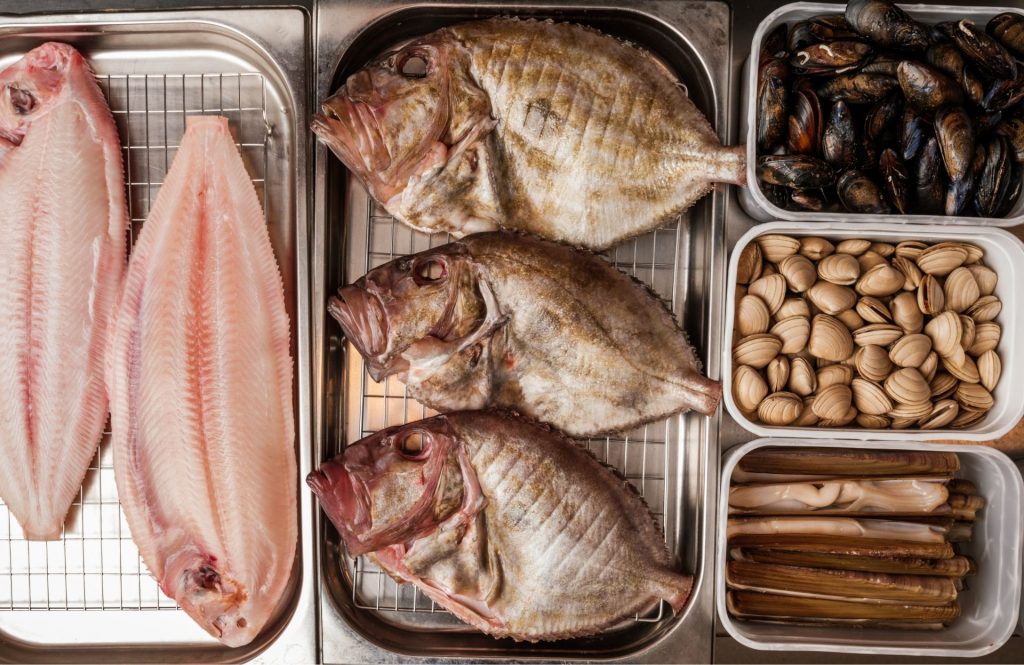 An assortment of fresh seafood arranged in trays, including filleted fish, whole fish, mussels and clams.
