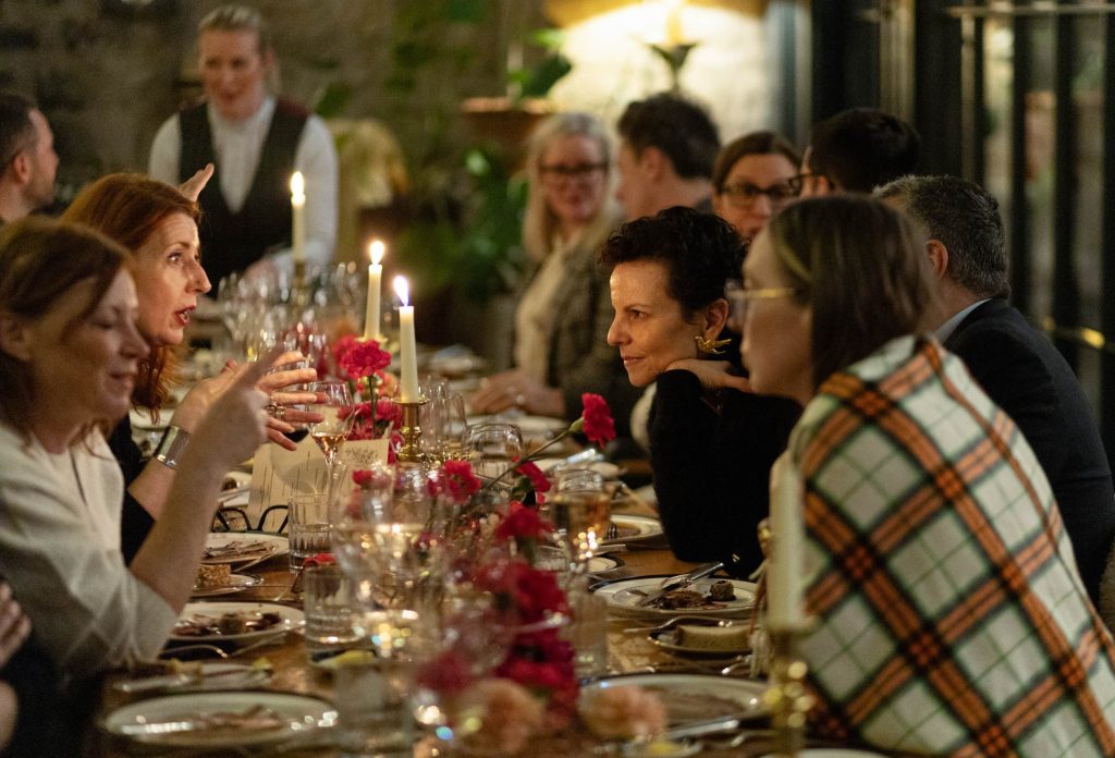 A group of women and men enjoying a luxurious dinner event seated at a long banquet table.