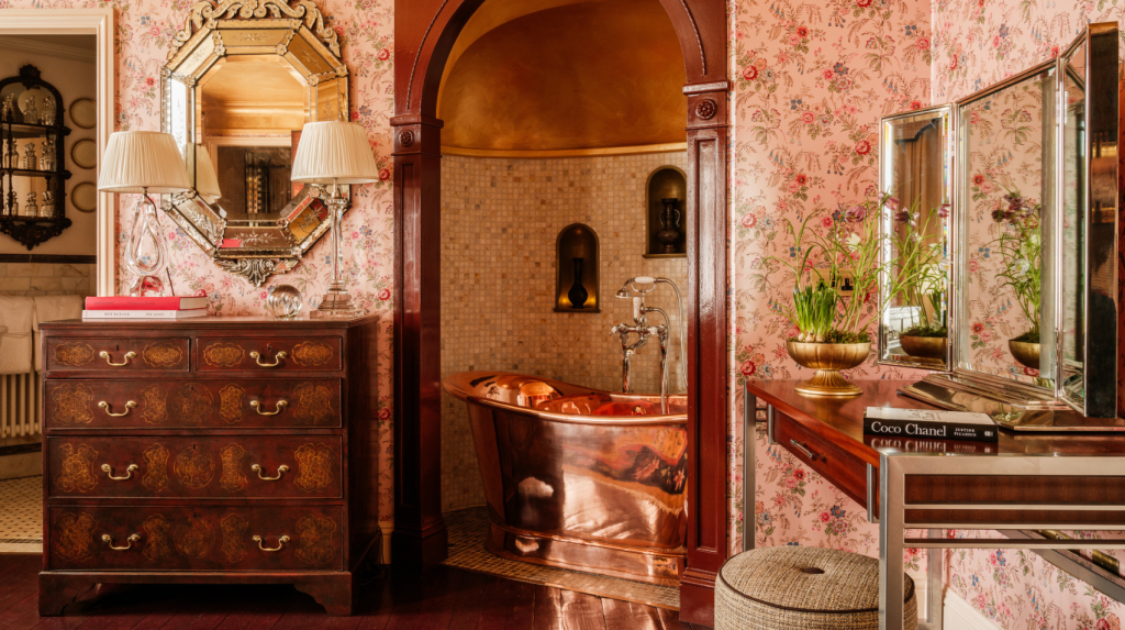 Copper bathtub in an arched tiled alcove within a the Secret Room, decorated with floral wallpaper.