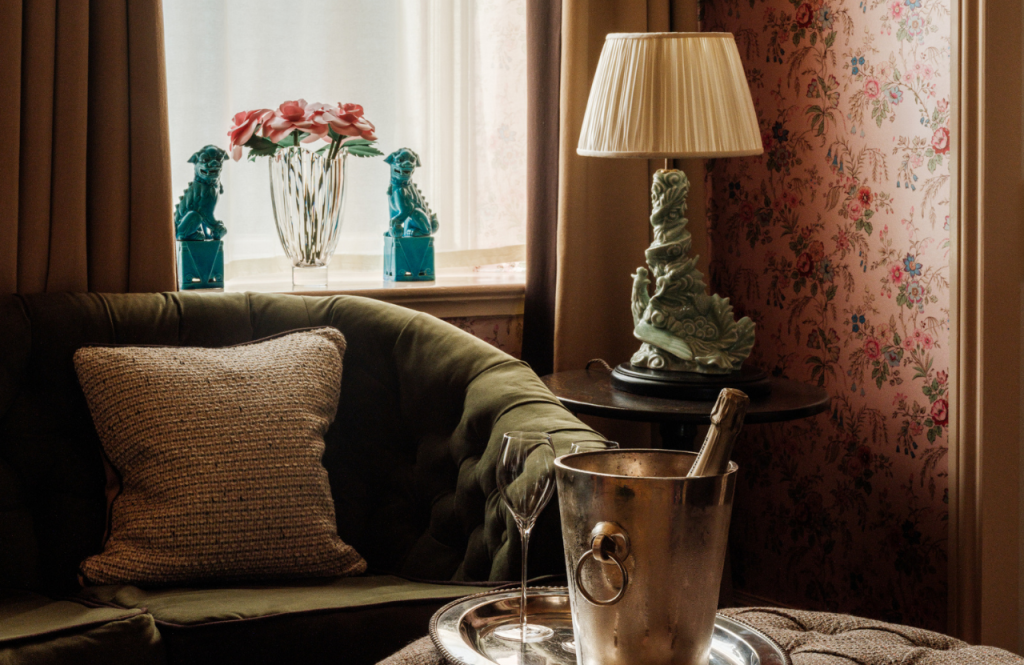 Cosy sitting area in Secret Room with a green velvet sofa, floral wallpaper, and a tray with a champagne bucket and glasses.