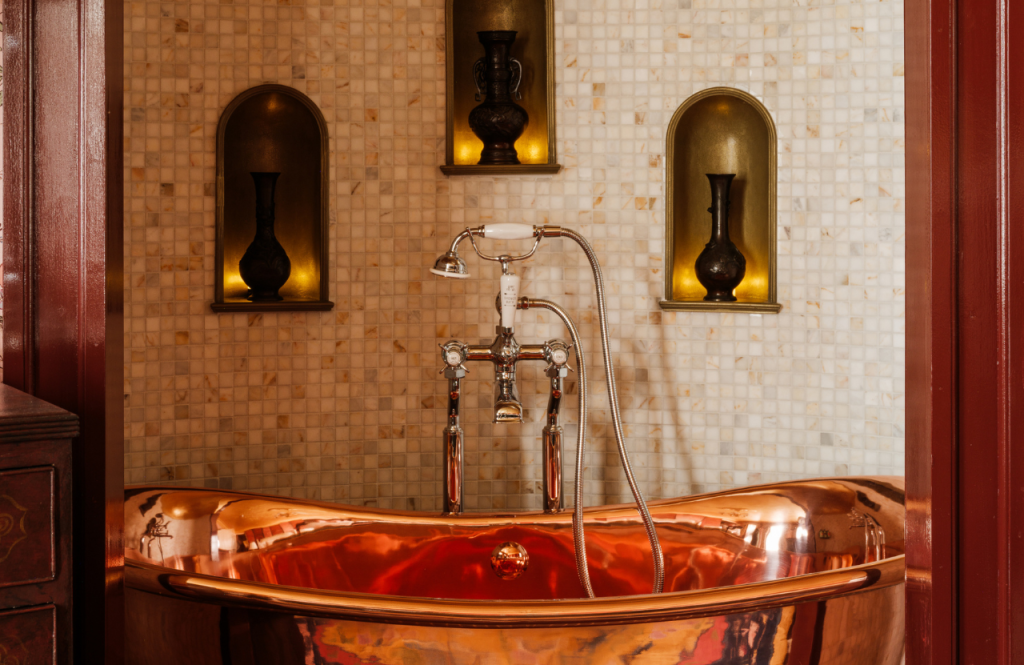 Secret Room copper bathtub in alcove beneath a tiled wall with three recessed alcoves holding decorative vases.