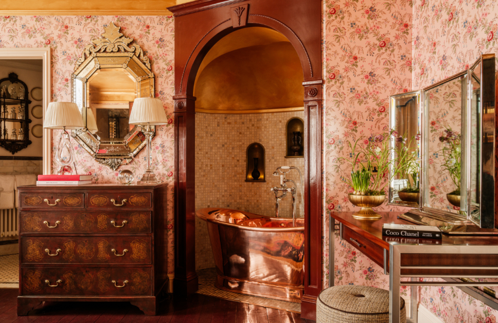 Copper bathtub in an arched tiled alcove within a the Secret Room, decorated with floral wallpaper.