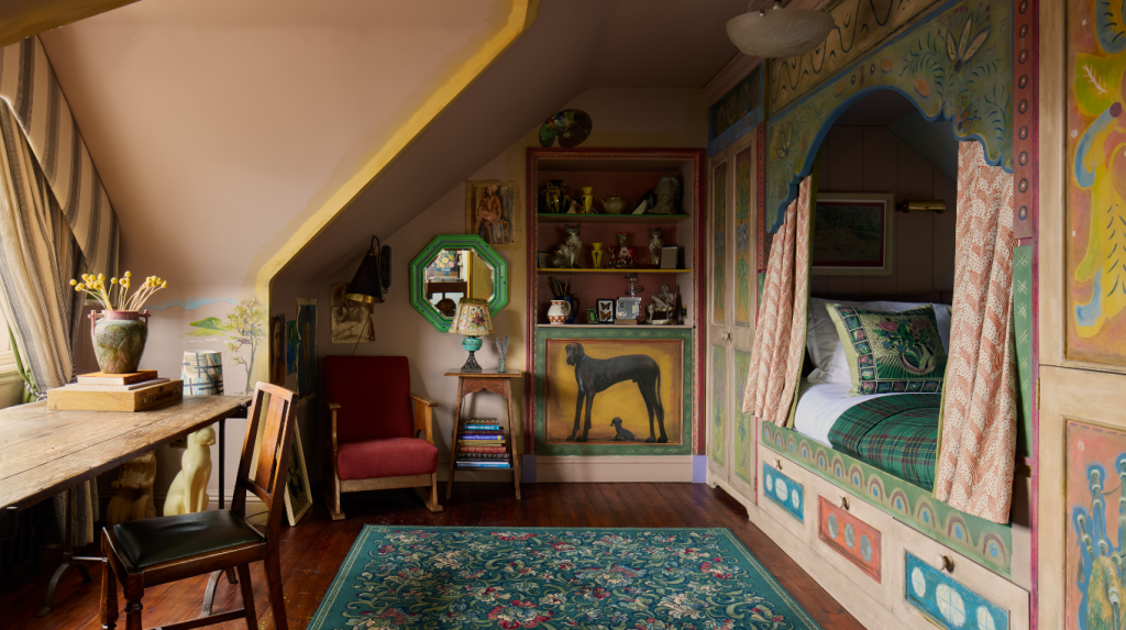Colourful Artist's Studio room featuring a painted alcove bed, wooden desk, and patterned rug.