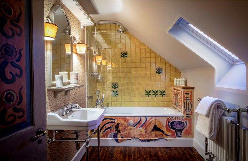 Artist's Studio bathroom with a yellow‑tiled bathtub, hand‑painted mural, and sloped ceiling skylight.