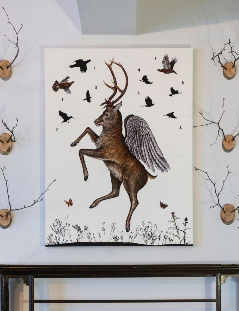 An illustration of a mythical stag with wings, surrounded by numbered birds and butterflies, displayed on a wall decorated with bare branches.