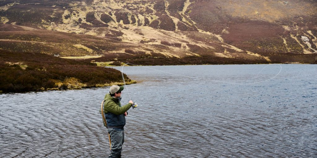 Fisherman fishing in a loch surrounded by scenic mountains