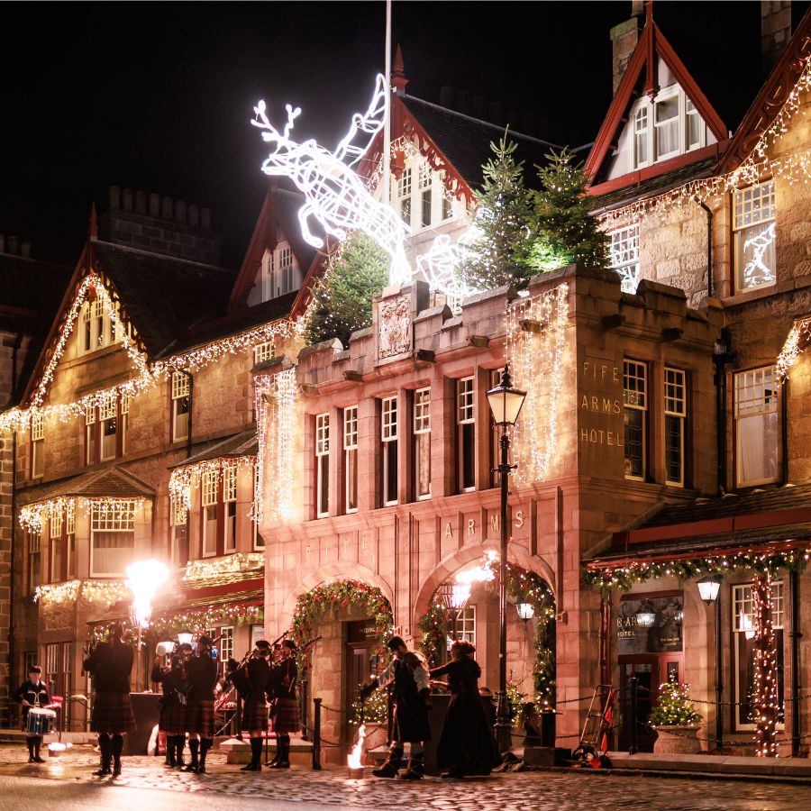 Exterior of the Fife Arms hotel lit up with festive lights and a pipe band playing