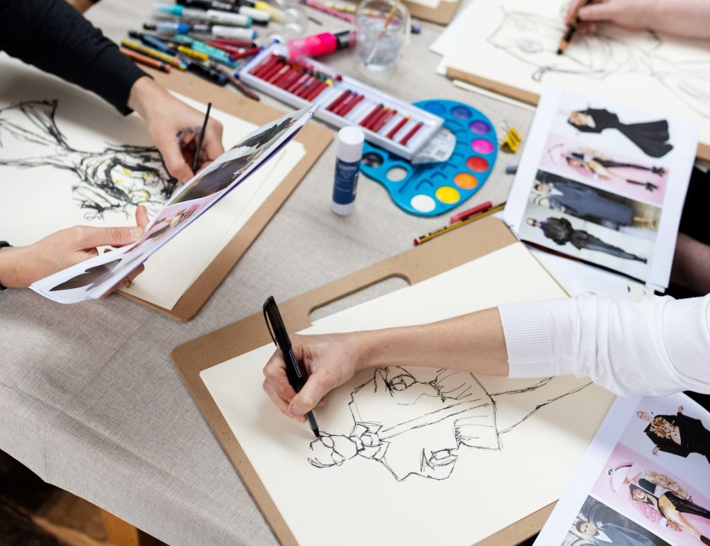Fashion illustration workshop during the festival of fashion weekend, with guests drawing models and art materials in the background