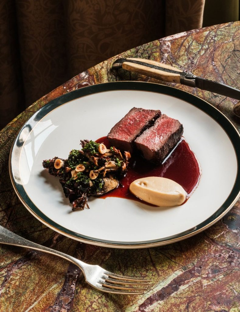 Beef steak cooked medium rare on a white plate at a dining room table with cutlery either side.