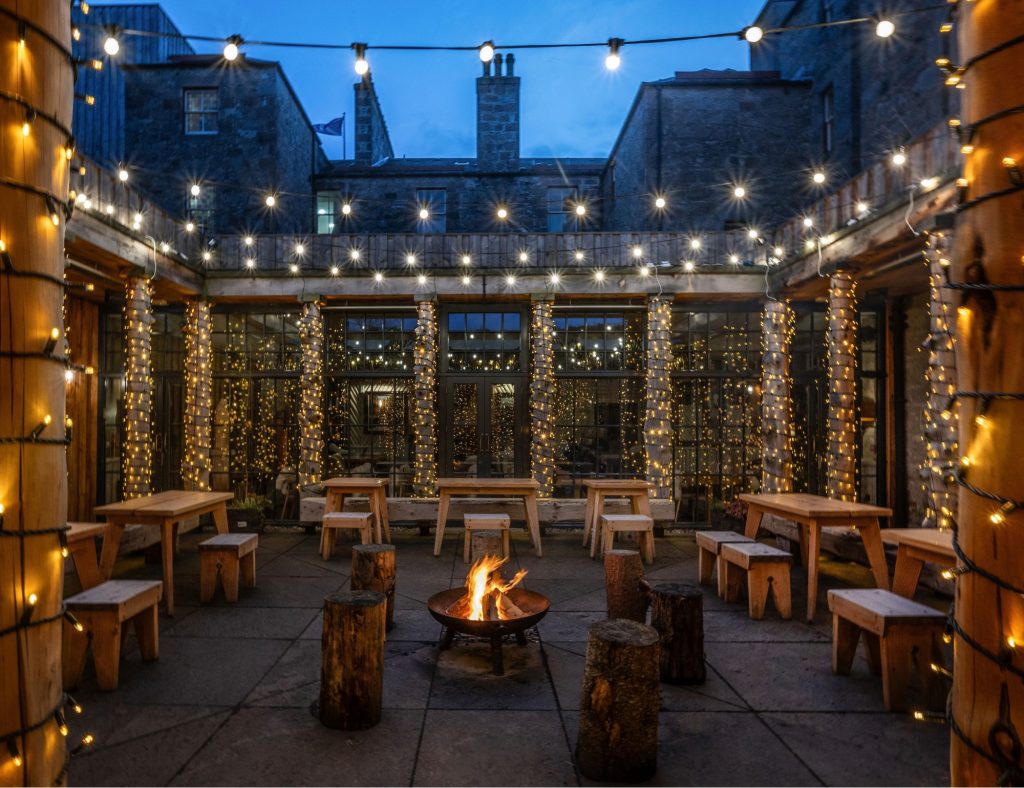 The Fife Arms courtyard at night with a fire pit lit and fairy lights adorning the walls.