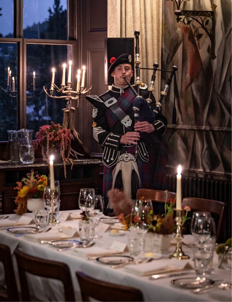 Bagpiper playing the pipes behind a dining table with lit candles.